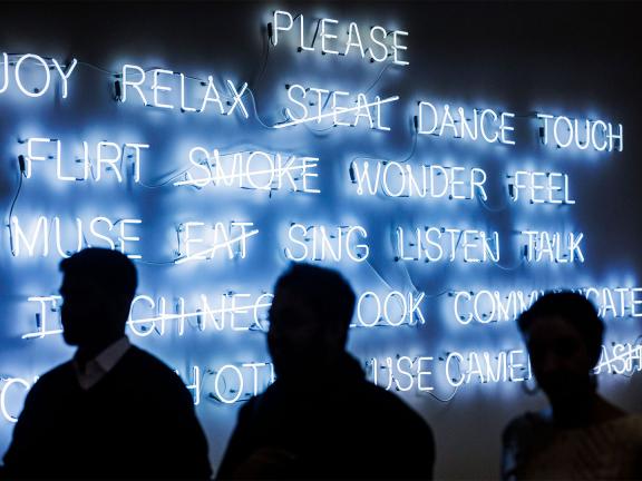 Silhouettes of three visitors in front of neon sign installation featuring words of actions one should or should not do in a museum