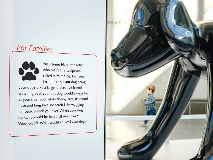 Large sculpture of thin black dog by Nara, in situ on stand in Shapiro Family Courtyard