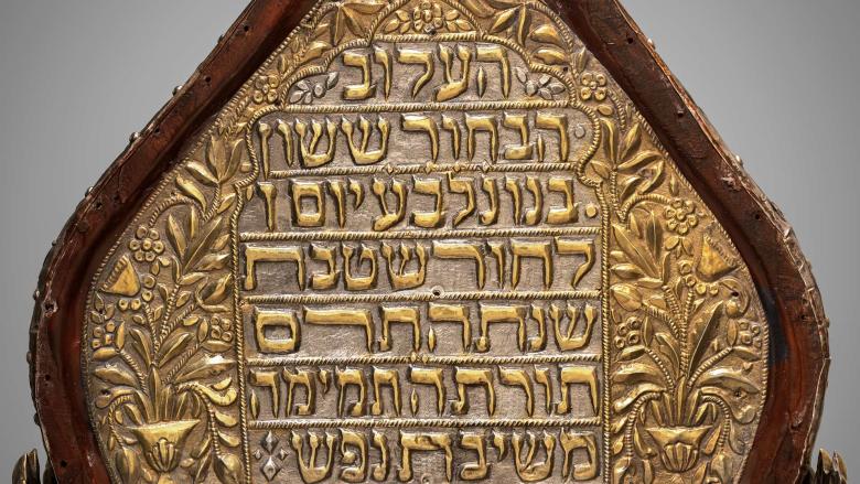 A wood and silver top of a Torah case with inscribed passages from the Torah. 