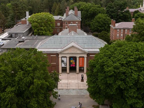 The facade of the Addison Gallery of American Art--a brick building with four columns surrounded by lush green trees