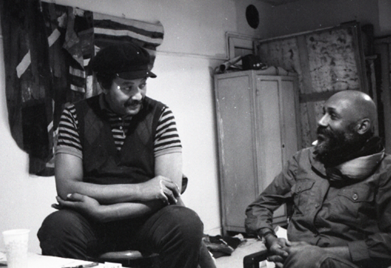 Black-and-white photo of two men sitting in an art studio.