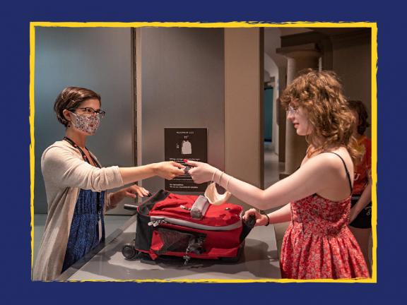 Visitor handing a bag to Museum staff person at coat check counter