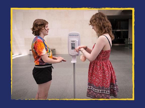 Two visitors applying hand sanitizer on their hand near hand sanitizer dispenser
