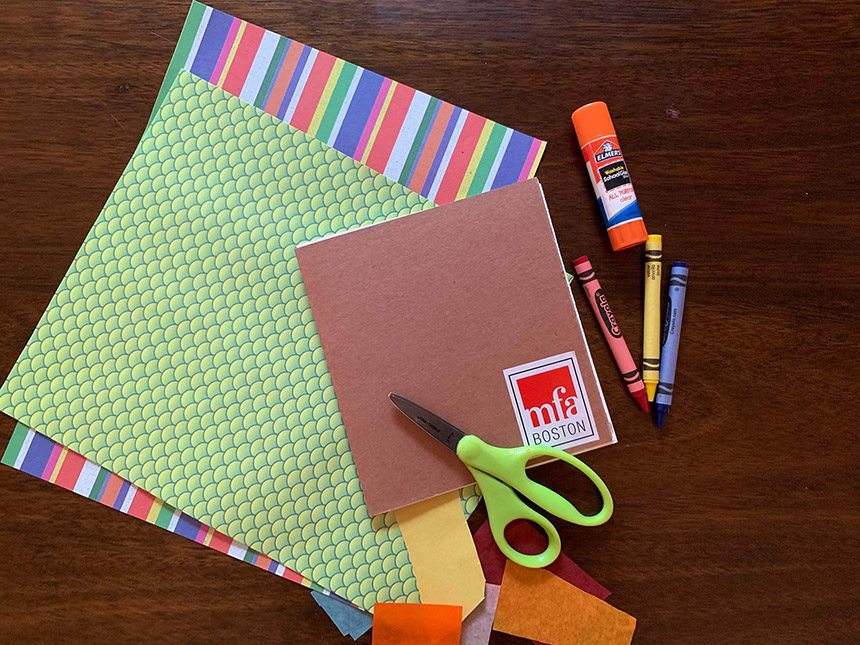 scissors, glue stick, crayons, and multicolored sheets of paper, all arranged on tabletop