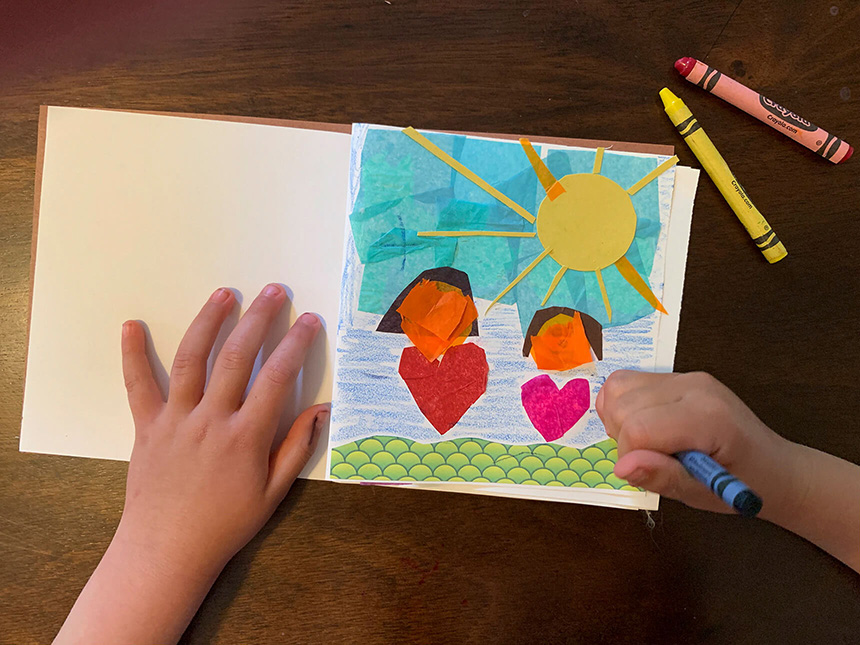 using crayons to color in areas around the glued on bits of paper to compose scene