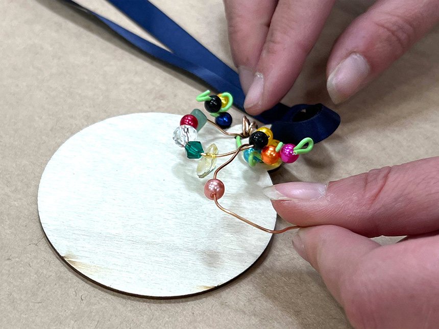 Tying ribbon through hole in pendant; beads tied to ribbon