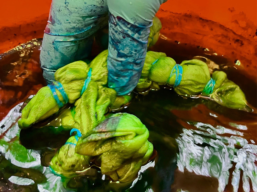 submerging white cloth bundle in dye mixture using rubber gloves