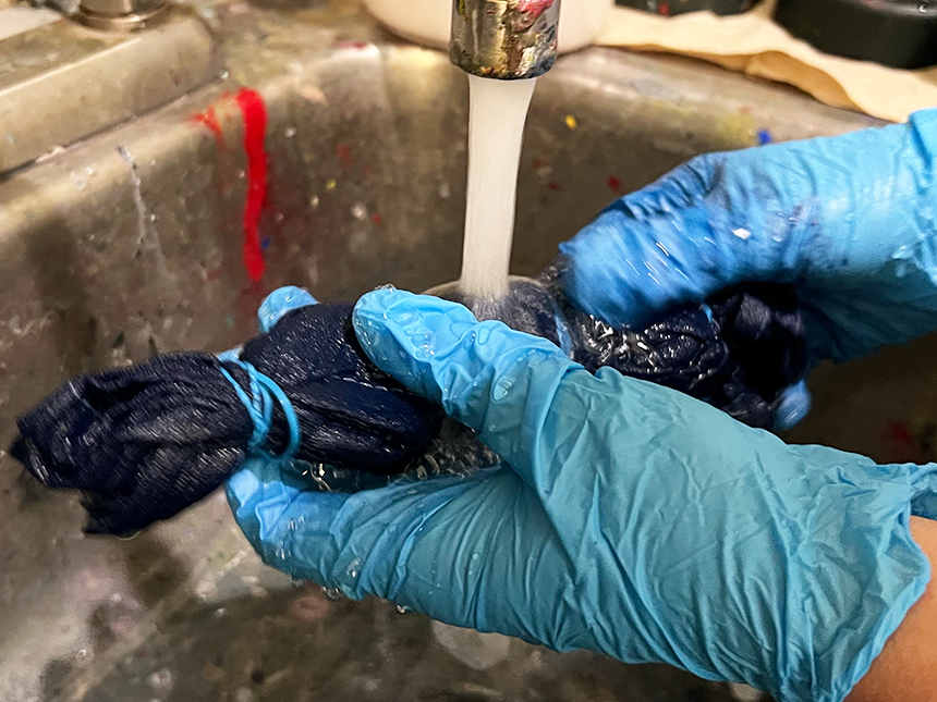 rinsing bundle of blue-dyed cloth underneath running water from faucet