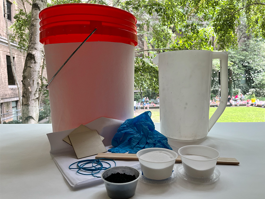 spread of plastic bucket, rubber gloves, cups with dyes and powders, a pitcher of water, and other materials