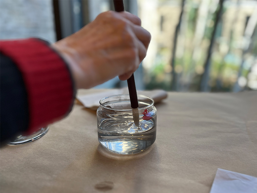 dipping ink brush into small glass jar of water
