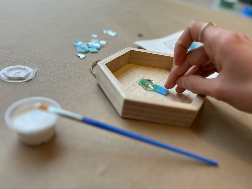 placing and arranging mosaic tiles inside pentagon-shaped wooden box