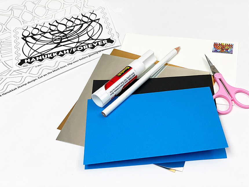 blue and silver cardstock laid on top of table with gluestick, white pencil, scissors, and menorah template