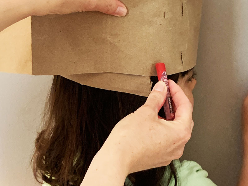 paper strip wrapped around child's head; adult marking off place to cut off excess