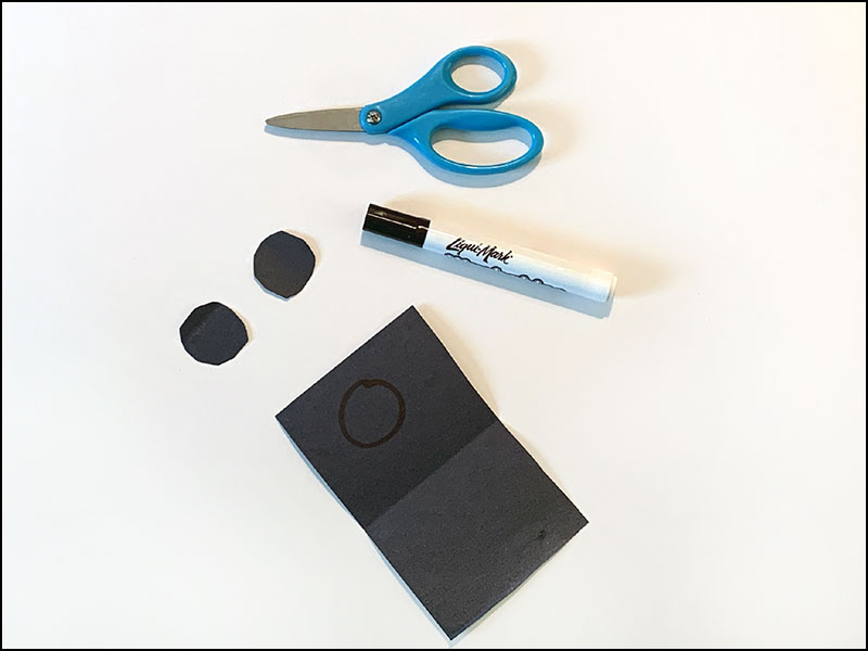 scissors and marker next to black construction paper with two circles cut out