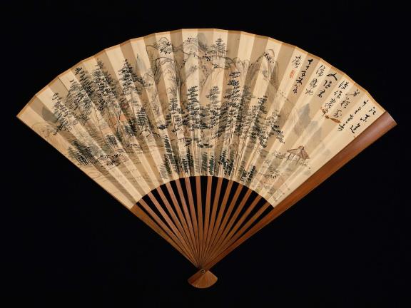 An opened Japanese folding fan reveals a detailed image of a landscape in ink 