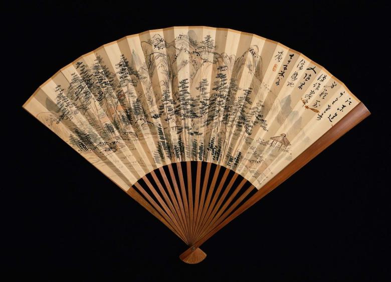 An opened Japanese folding fan reveals a detailed image of a landscape in ink 