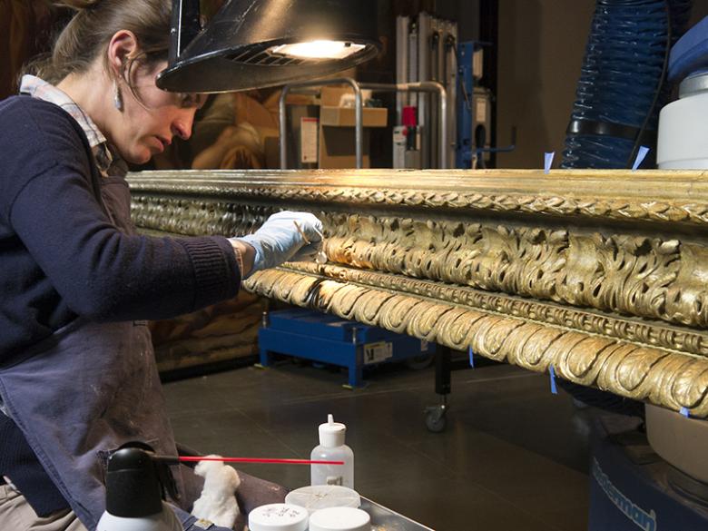 Conservator cleaning gilding on an oversized frame