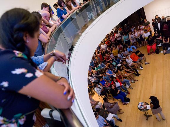 Visitors looking down from second floor of Linde Family Wing, watching speaker in front of seated crowd during City Talk
