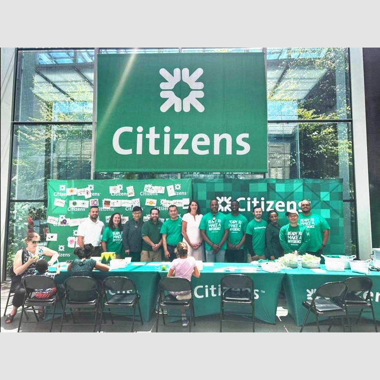 Staff from Citizens tabling at open house event, gathered underneath large Citizens banner