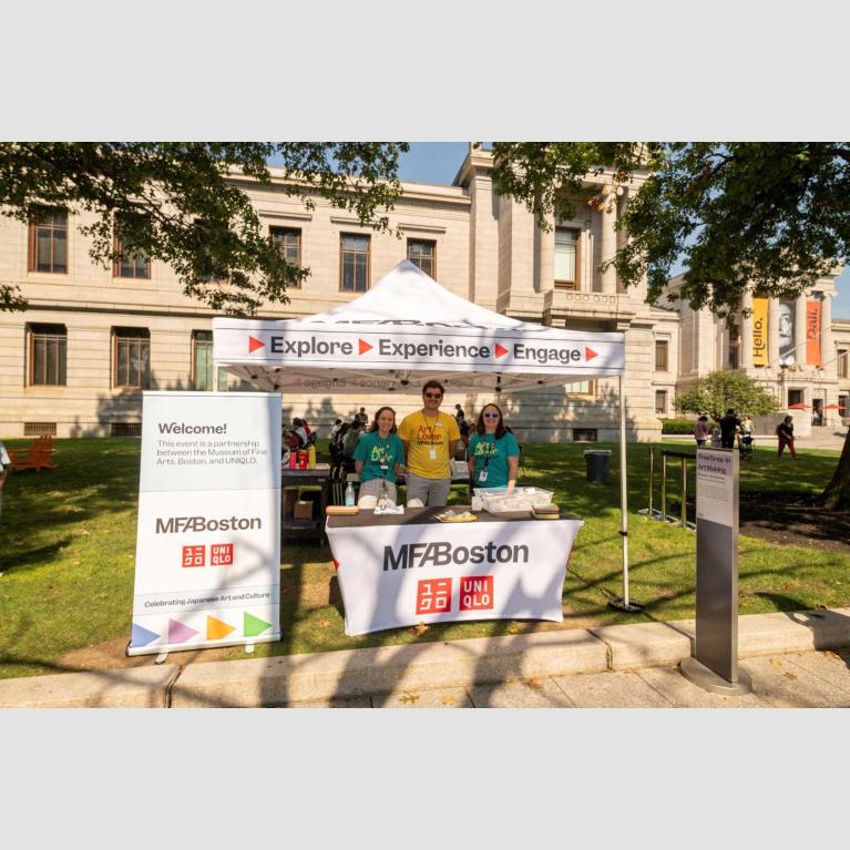 Museum staff standing under tent set up for art making activity outside Museum