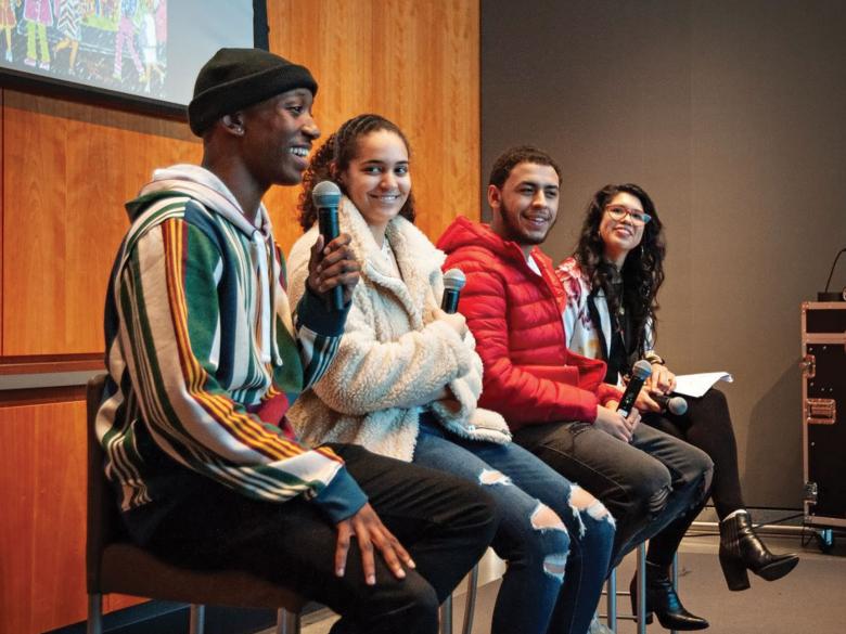 Three teens with microphones sitting on high stools in front of projection screen with curator