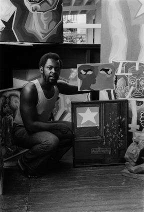 Black and white photo of a man kneeling in front of a number of painted canvases.