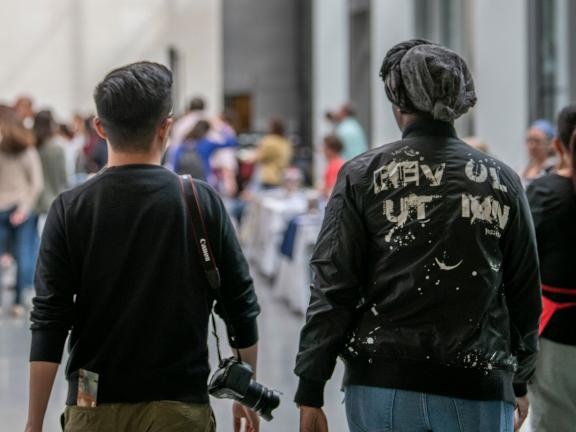 Backs of two visitors in Shapiro Family Courtyard, walking, camera slung on shoulder of one visitor