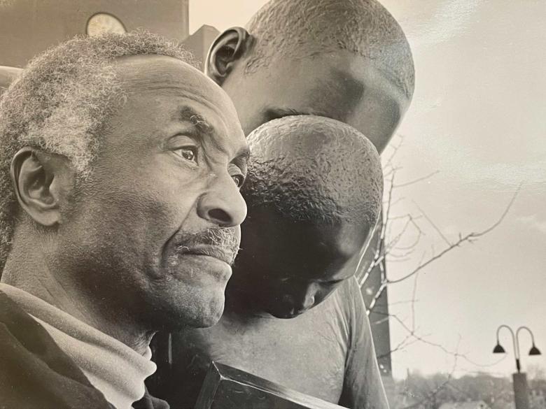 Artist John Wilson stands in front of his sculpture of a father and child reading.