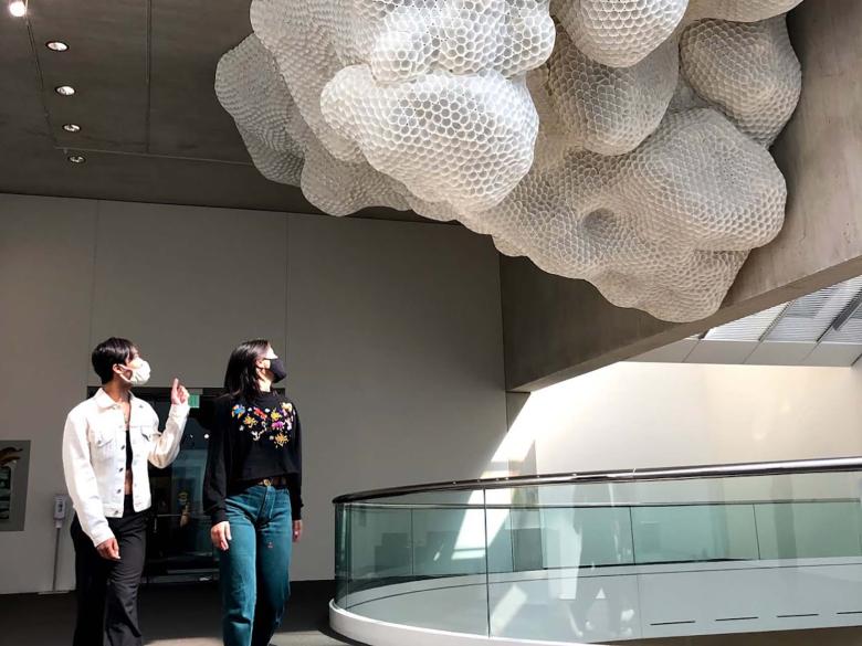 Two visitors looking at cloud-like sculpture suspended from ceiling of Linde Family Wing