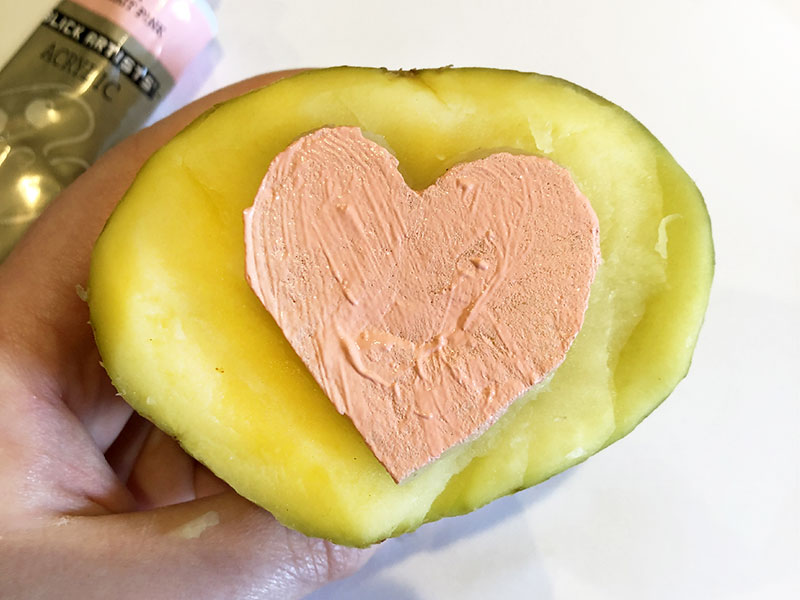 pink paint applied to surface of carved out heart on potato half