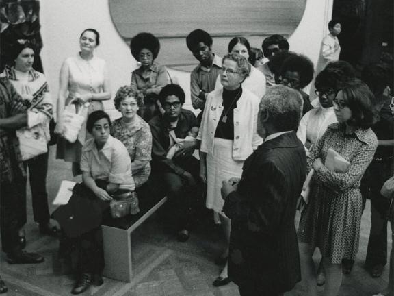 A crowd of people gathers around a man in an art gallery.