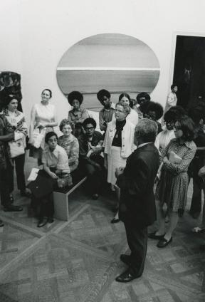 A crowd of people gathers around a man in an art gallery.