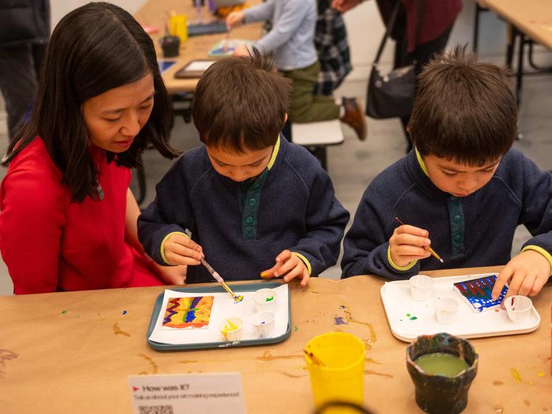 Mayor Michelle Wu sits with two young sons, painting on paper at long table