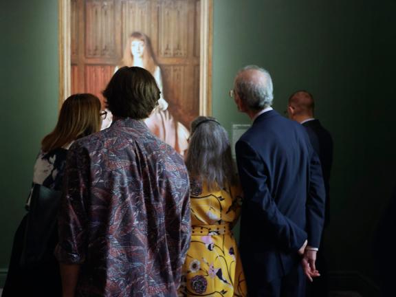 Visitors in "Fashioned by Sargent" exhibition, gathered closely around portrait of a young girl in a dress