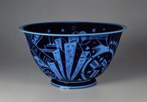 A glazed, black porcelain bowl is decorated with brilliant blue incised motifs of New York City attractions
