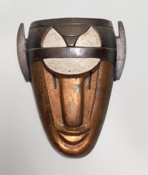 A copper and enamel mask mimicking a human face wears a white and dark brown headpiece.
