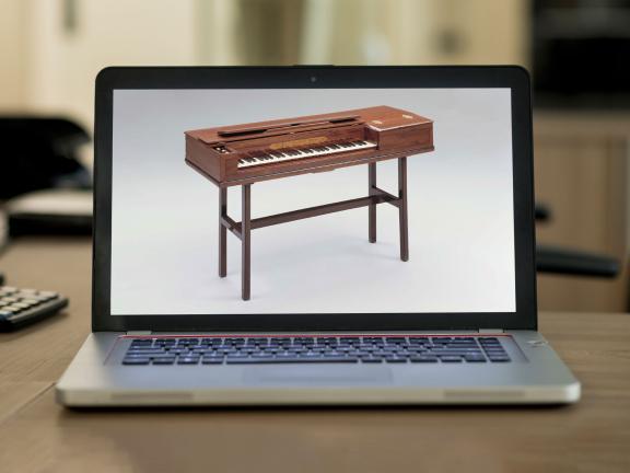 A laptop computer on a desk displays an image of an 18th-century wood piano