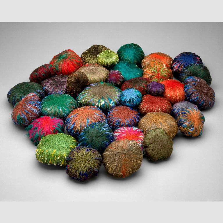 Thirty-six wrapped bundles of polychrome yarns wound around miscellaneous objects.