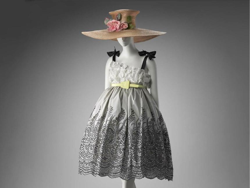 mannequin modeling evening dress with intricate gray pattern on skirt, black bows on shoulder strap, topped off with large straw hat