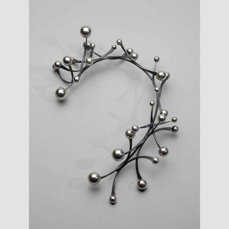 A photograph of a rigid, silver necklace decorated with thin metal pieces that have silver balls on each end.