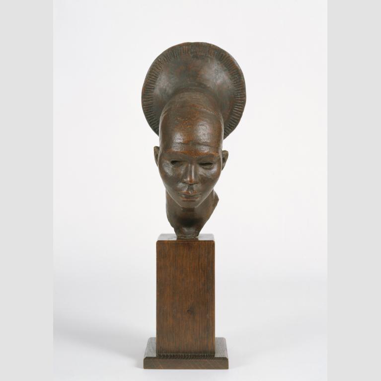 A brown, metallic-looking sculpture of a woman's head, headpiece, and neck on a wood base