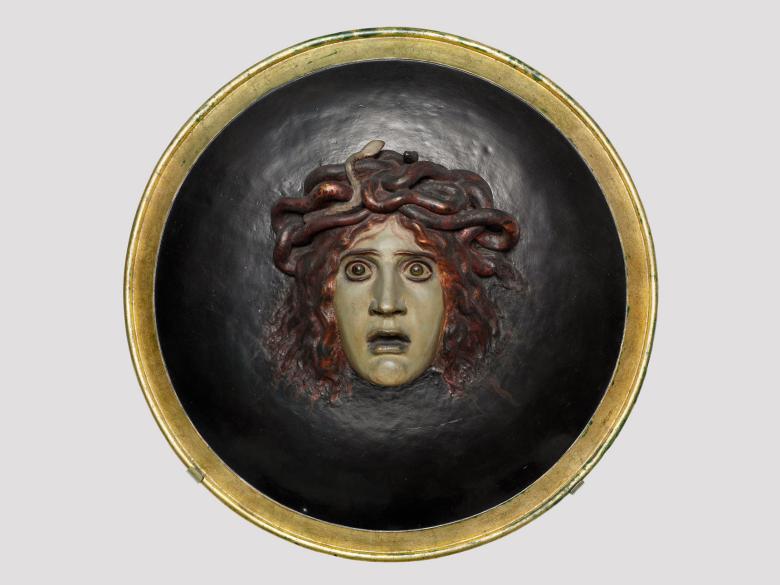 Circular relief sculpture of Medusa with a fearful expression on a black background