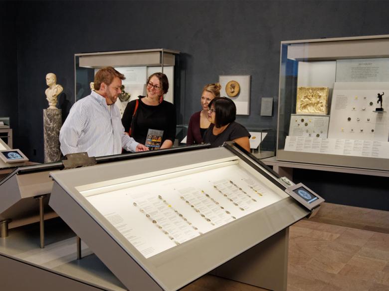 Four visitors standing behind large case of ancient coins in gallery