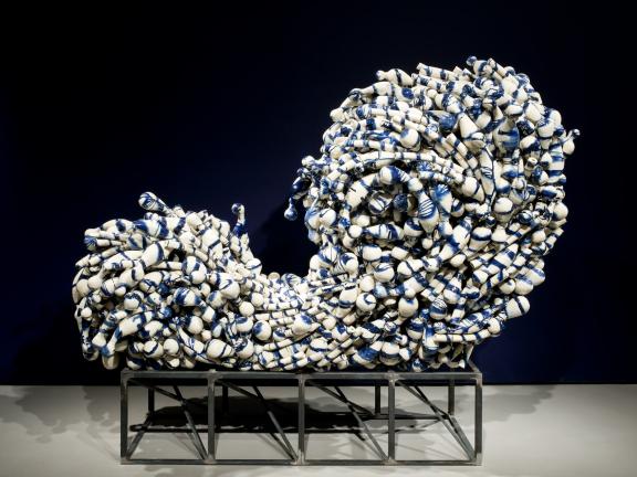 A group of amorphous blue-and-white ceramics are wired together in the shape of a cresting wave.