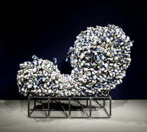 A group of amorphous blue-and-white ceramics are wired together in the shape of a cresting wave.