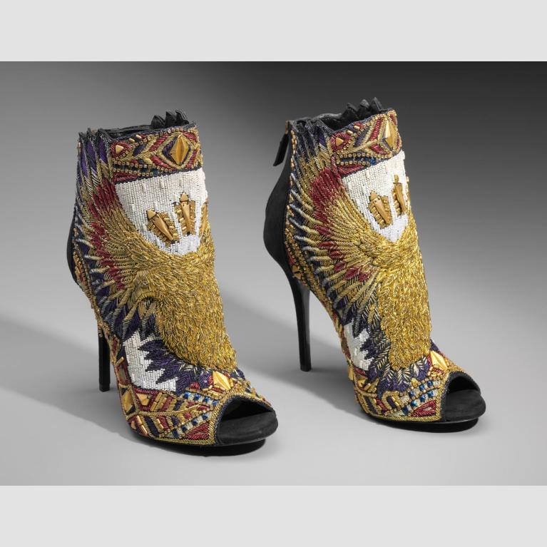 A pair of black suede heeled booties embroidered with a double-headed eagle in gold, red, and blue on the center front with wings extending upwards towards the back of the shoes. 