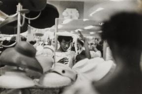A woman looks in a department store mirror as she tries on a hat for sale.