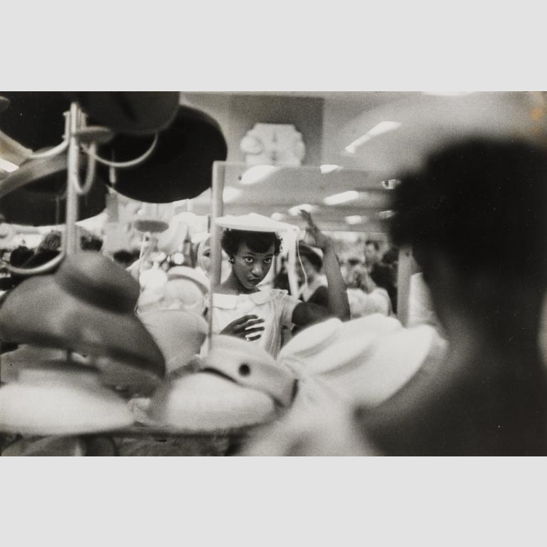 A woman looks in a department store mirror as she tries on a hat for sale.