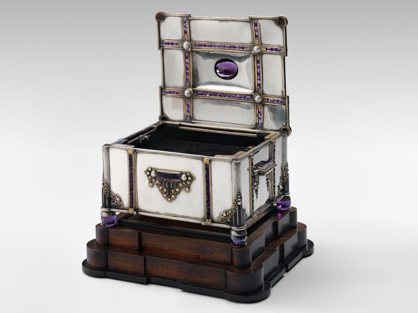 silver box with inlaid jewels on a dark wood base