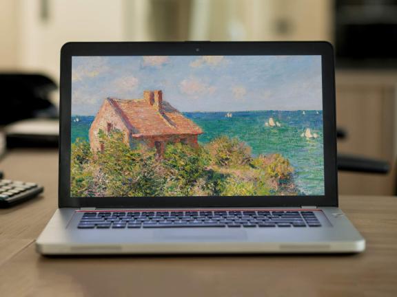 A laptop computer on a desk shows a landscape painting by Monet on its screen